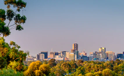 Adelaide byskyline med skyskrabere og groenne bakker under solnedgang