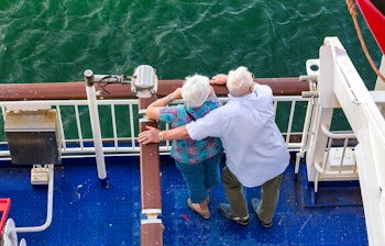 Ældre par nyder udsigten fra krydstogtskibets dæk med armene om hinanden på en afslappende ferieoplevelse