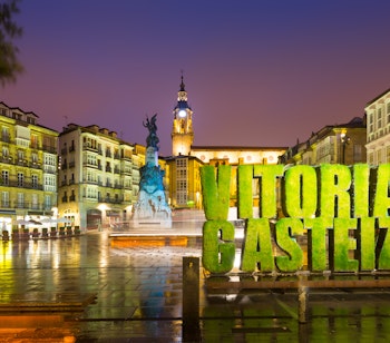 Stemningsfuld aftenbelysning på det historiske Virgen Blanca torv i Vitoria-Gasteiz med byens ikoniske grønne byskilt