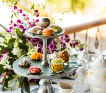Klassisk engelsk afternoon tea med kager på etagere, vintage porcelænskopper og friske blomster serveret i idylliske omgivelser i Kensington Gardens