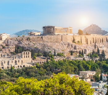 Panoramaudsigt over Akropolis-højen med Parthenon-templet i Athen på en solrig sommerdag med blå himmel og bylandskab i baggrunden