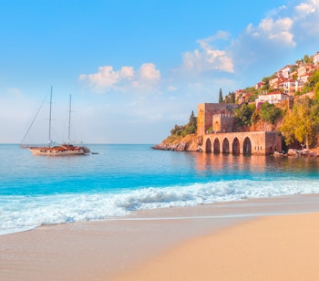 Idyllisk sandstrand med turkisblåt Middelhav ved det historiske skibsværft nær Kizil Kule-tårnet i Alanya, Tyrkiet