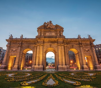 En neoklassisk monument, Alcala-porten, oplyst om natten i Plaza de la Independencia, Madrid, som viser historisk arkitektur.