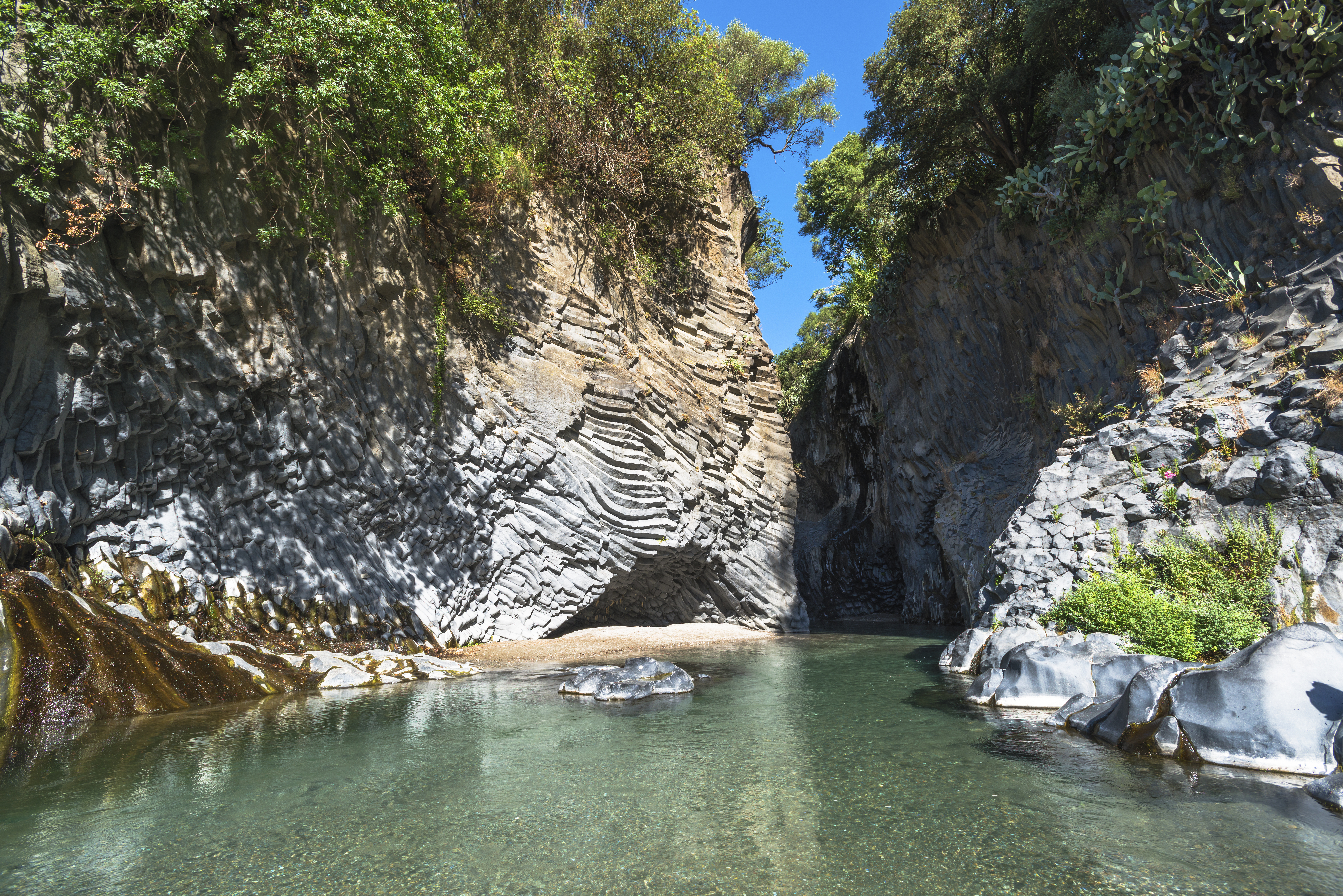 Den imponerende Alcantara-kløft på Sicilien med krystalklart turkisblåt vand der strømmer gennem dramatiske vulkanske klippeformationer