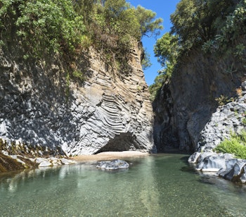 Den imponerende Alcantara-kløft på Sicilien med krystalklart turkisblåt vand der strømmer gennem dramatiske vulkanske klippeformationer