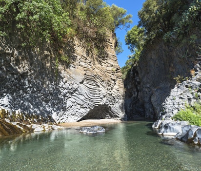 Den imponerende Alcantara-kløft på Sicilien med krystalklart turkisblåt vand der strømmer gennem dramatiske vulkanske klippeformationer