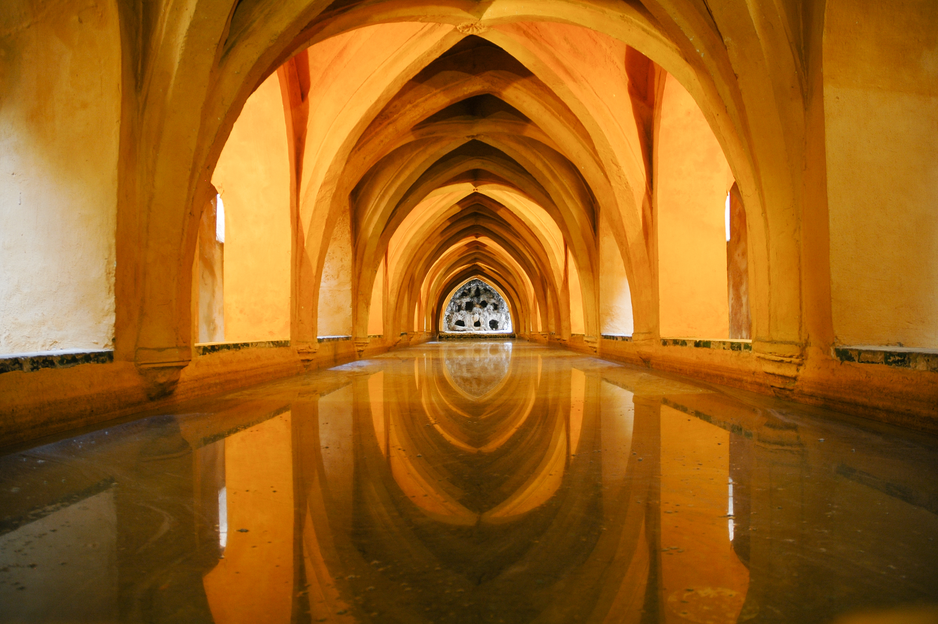 Gylden buegange med vandrefleksion i Alcazar paladsets badesal i Sevilla, Spanien