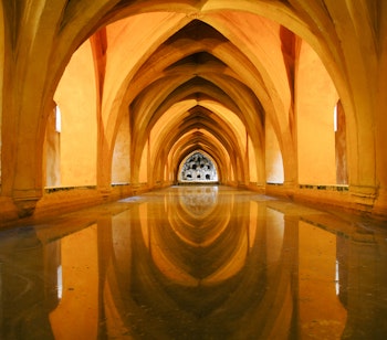 Gylden buegange med vandrefleksion i Alcazar paladsets badesal i Sevilla, Spanien