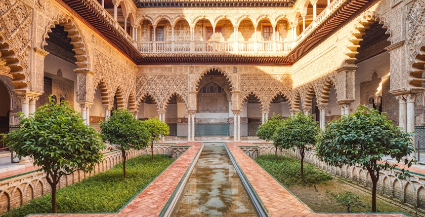 Smuk gårdhave i det kongelige Alcazar-palads i Sevilla med elegante søjler, mauriske buer og detaljerede dekorationer - oplev Andalusiens fascinerende blanding af islamisk og spansk arkitektur på din rejse til Spanien