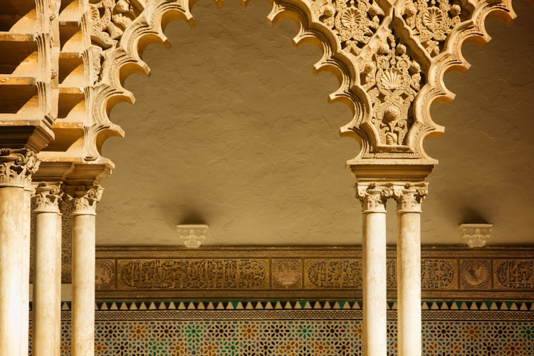 Smukke mauriske buer og udskåret stendekoration i Alcazar paladsets gård i Sevilla, Spanien