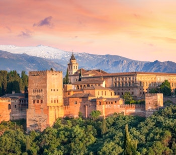 Det historiske mauriske Alhambra-palads badet i gyldent aftenlys med Sierra Nevada-bjergene i baggrunden, Granada, Andalusien