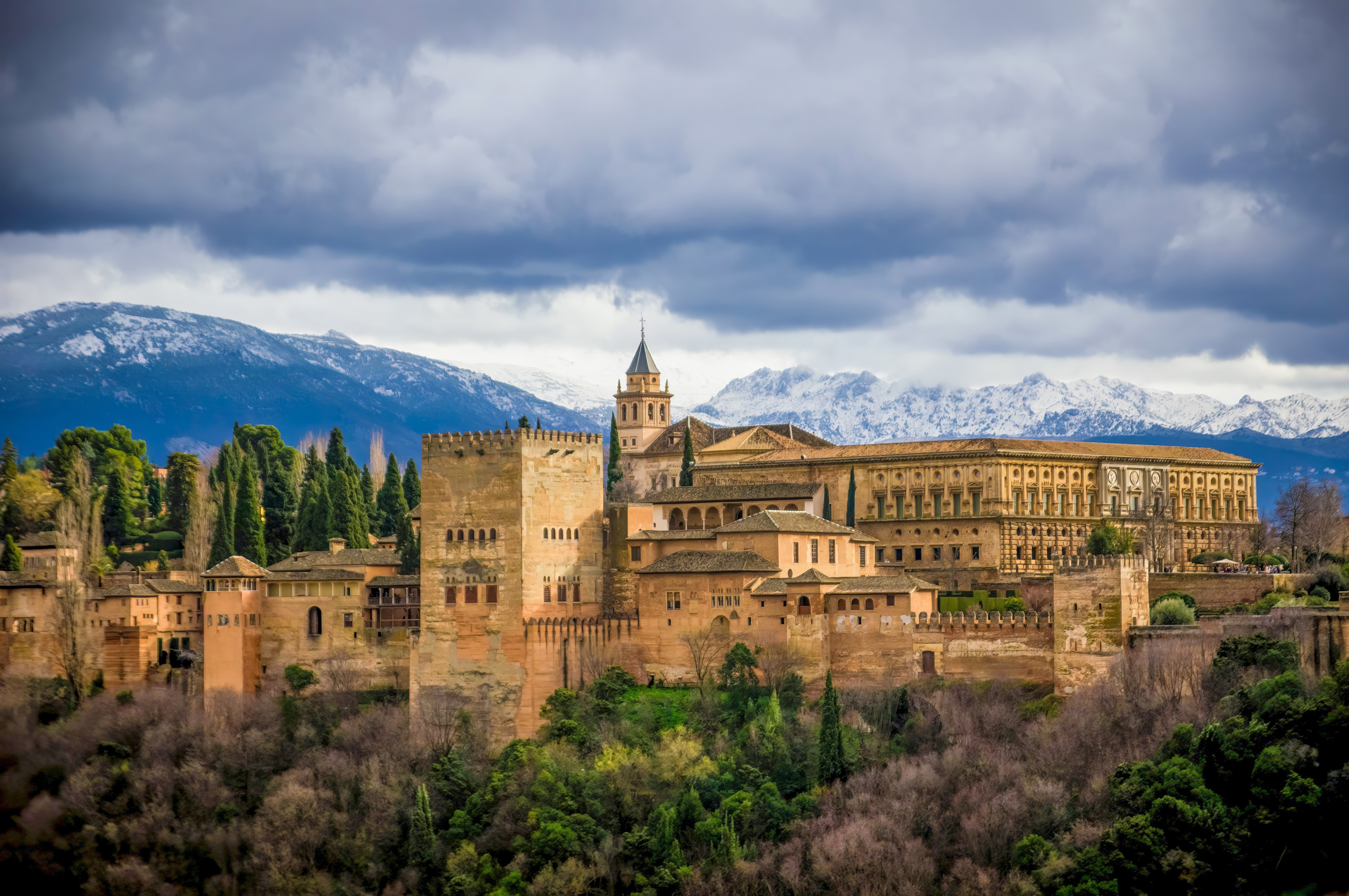 Det historiske Alhambra-palads i Granada, Andalusien med smuk maurisk arkitektur og sneklædte bjerge i baggrunden under dramatisk himmel