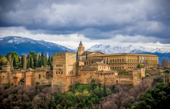 Det historiske Alhambra-palads i Granada, Andalusien med smuk maurisk arkitektur og sneklædte bjerge i baggrunden under dramatisk himmel