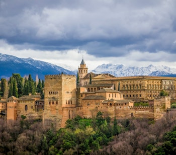 Det historiske Alhambra-palads i Granada, Andalusien med smuk maurisk arkitektur og sneklædte bjerge i baggrunden under dramatisk himmel