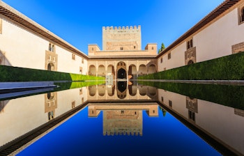 Alhambra-paladset i Granada med det smukke mauriske vandbassiner der reflekterer den historiske arkitektur under en klar blå himmel