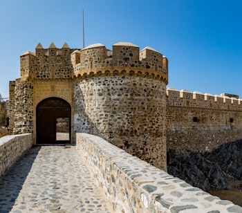 Panoramaudsigt over det historiske Almuñécar-slot med stenporte og tårne under blå himmel i Andalusien, Spanien