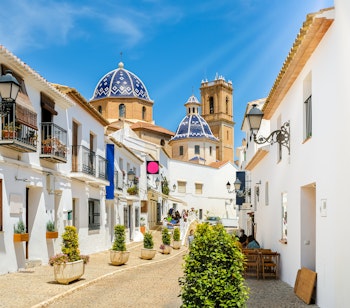 Charmerende gade i Alteas gamle bydel med traditionelle hvide huse og den ikoniske blå kuppelkirke Vor Frue af Trøst, Costa Blanca, Spanien