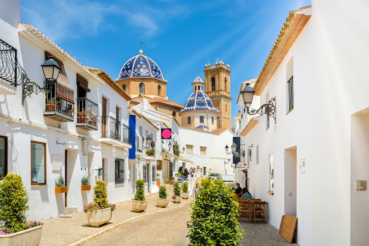 Charmerende gade i Alteas gamle bydel med traditionelle hvide huse og den ikoniske blå kuppelkirke Vor Frue af Trøst, Costa Blanca, Spanien