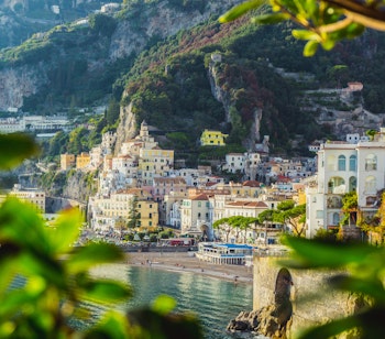 Betagende panoramaudsigt over den historiske by Amalfi i Campania, med farverige bygninger der trapper ned ad bjergsiden mod den blå Middelhavsbugt og de karakteristiske klipper