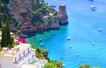 Idyllisk udsigt over den farverige Amalfi-kyst i Italien med traditionelle huse på klippeskrænter, blomstrende bougainvillea og både på det azurblå Middelhav