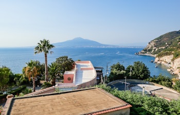Malerisk udsigt over Amalfi-kysten ved Vico Equense med vulkanen Vesuv i baggrunden og sejlbåde på det azurblå Middelhav i sommersolen
