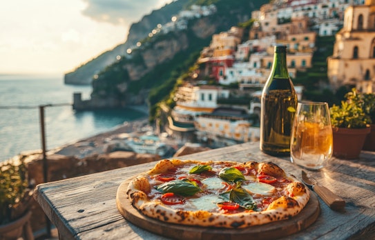 Italiensk pizza med mozzarella og basilikum på træbord med udsigt over Amalfikysten ved solnedgang