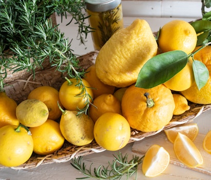 Friske gule citroner og rosmarin i en kurv på hvidt træbord - symboliserer Amalfikystens berømte citrusfrugter og det lokale italienske køkken