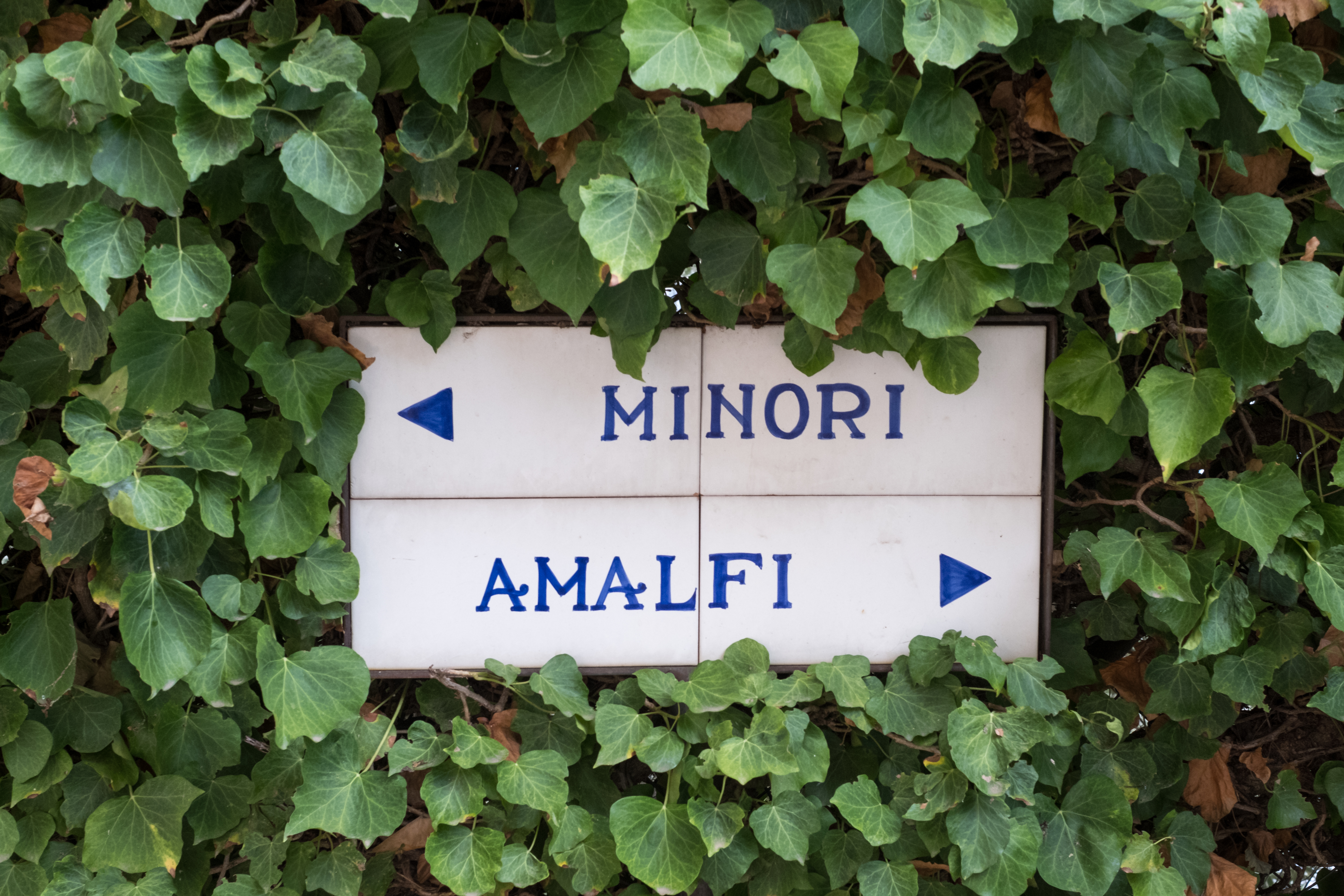 Vejskilt på vandreruten i Dragedalene mellem Ravello og Atrani, der viser vej til Minori og Amalfi, omgivet af frodigt grønt løv på Italiens berømte Amalfikyst