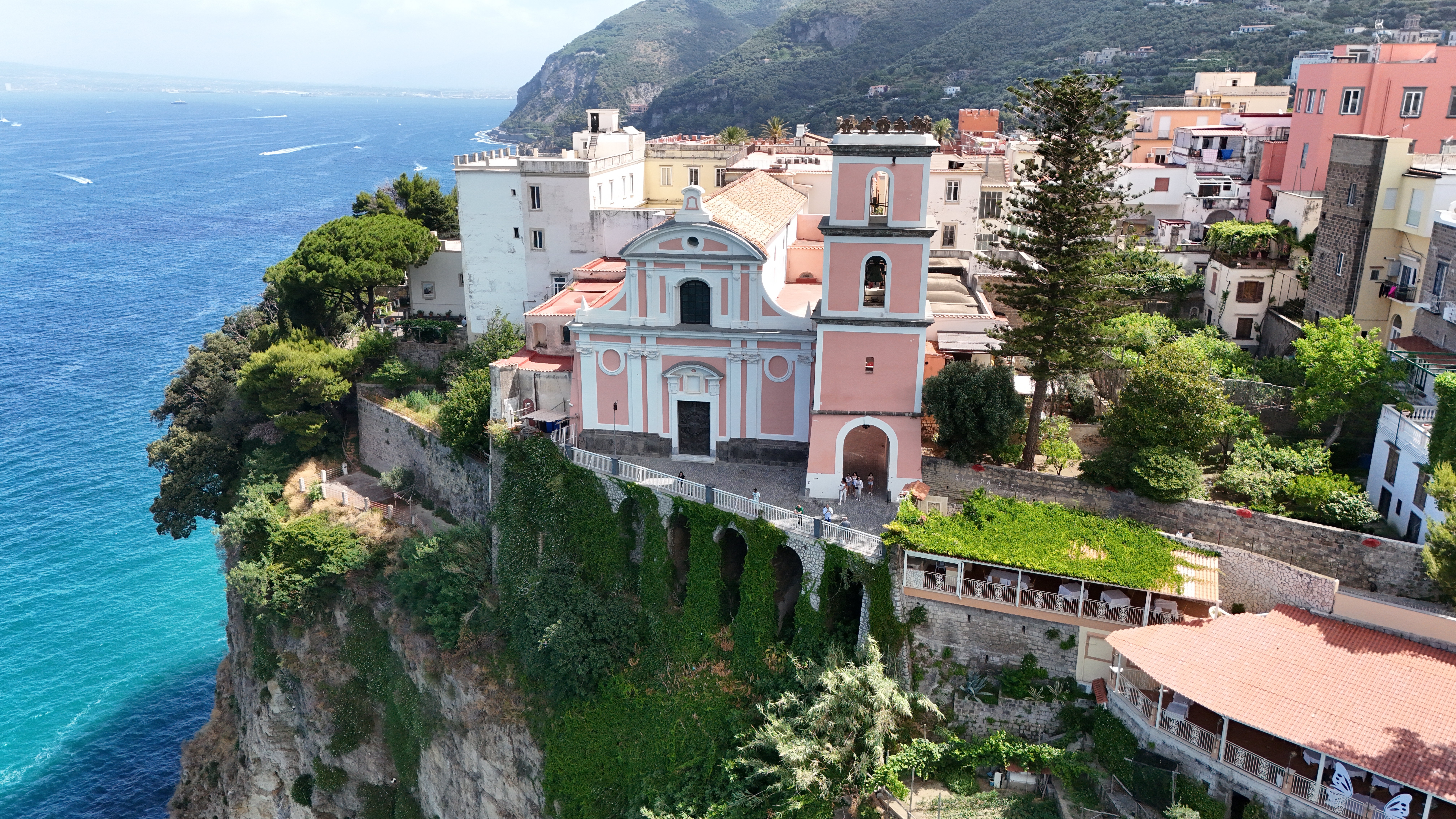 Fantastisk luftfoto af farverig italiensk kystby med pink kirke ved Middelhavet og dramatiske klipper