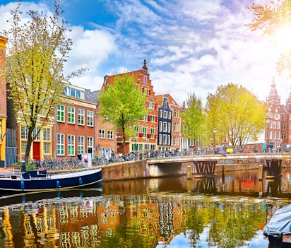 Idyllisk kanalvy i Amsterdam med historiske huse langs Amstel-floden der spejler sig i vandet om foråret
