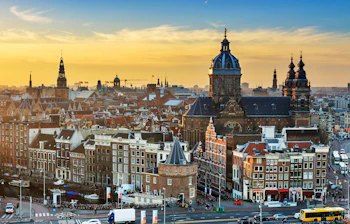 Stemningsfuld vintersolnedgang over Amsterdams historiske skyline med traditionel hollandsk arkitektur silhuet mod den gyldne aftenhimmel