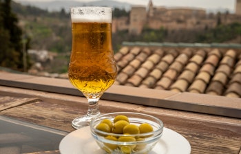 Spansk øl og grønne andalusiske oliven serveret på terrasse med udsigt til Sierra Nevada-bjergene i Granada, Spanien