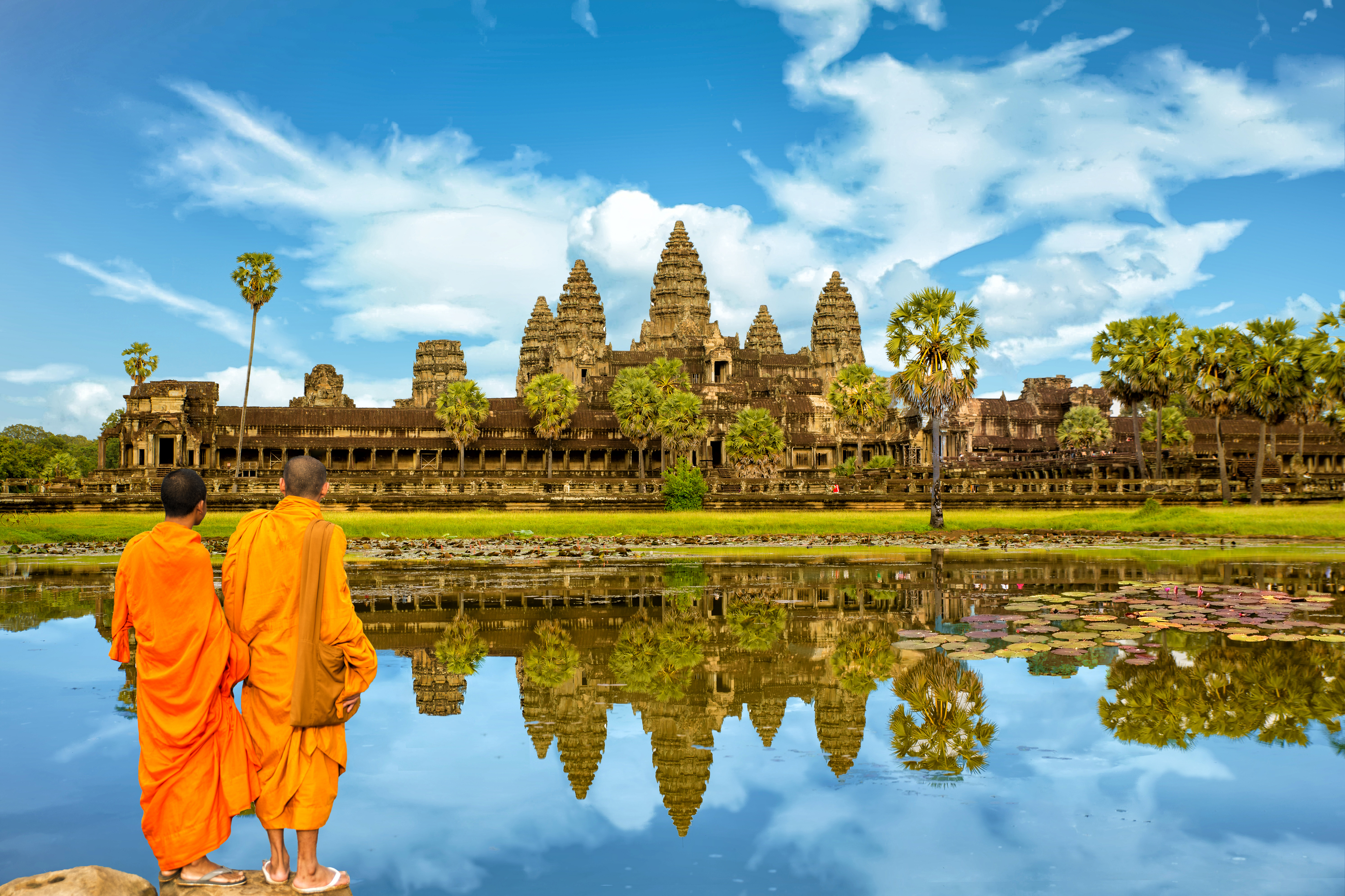Buddhistische munke i orange gevandter betragter Angkor Wat tempelkompleks spejlet i vandet ved solopgang i Cambodja