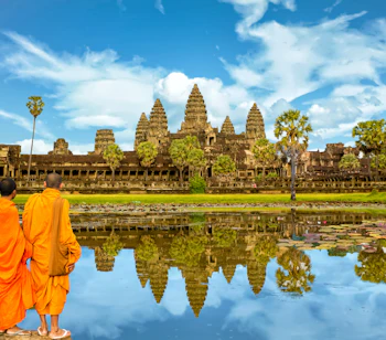 Buddhistische munke i orange gevandter betragter Angkor Wat tempelkompleks spejlet i vandet ved solopgang i Cambodja