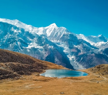 Betagende isblå sø på Annapurna-ruten i Himalaya, Nepal, med sneklædte bjergtinder under klar himmel - perfekt til eventyrlige vandrere