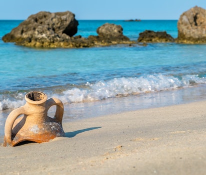 Antik græsk amfora på den sandede Elafonissi strand på Kreta med turkisblåt vand og klipper i baggrunden