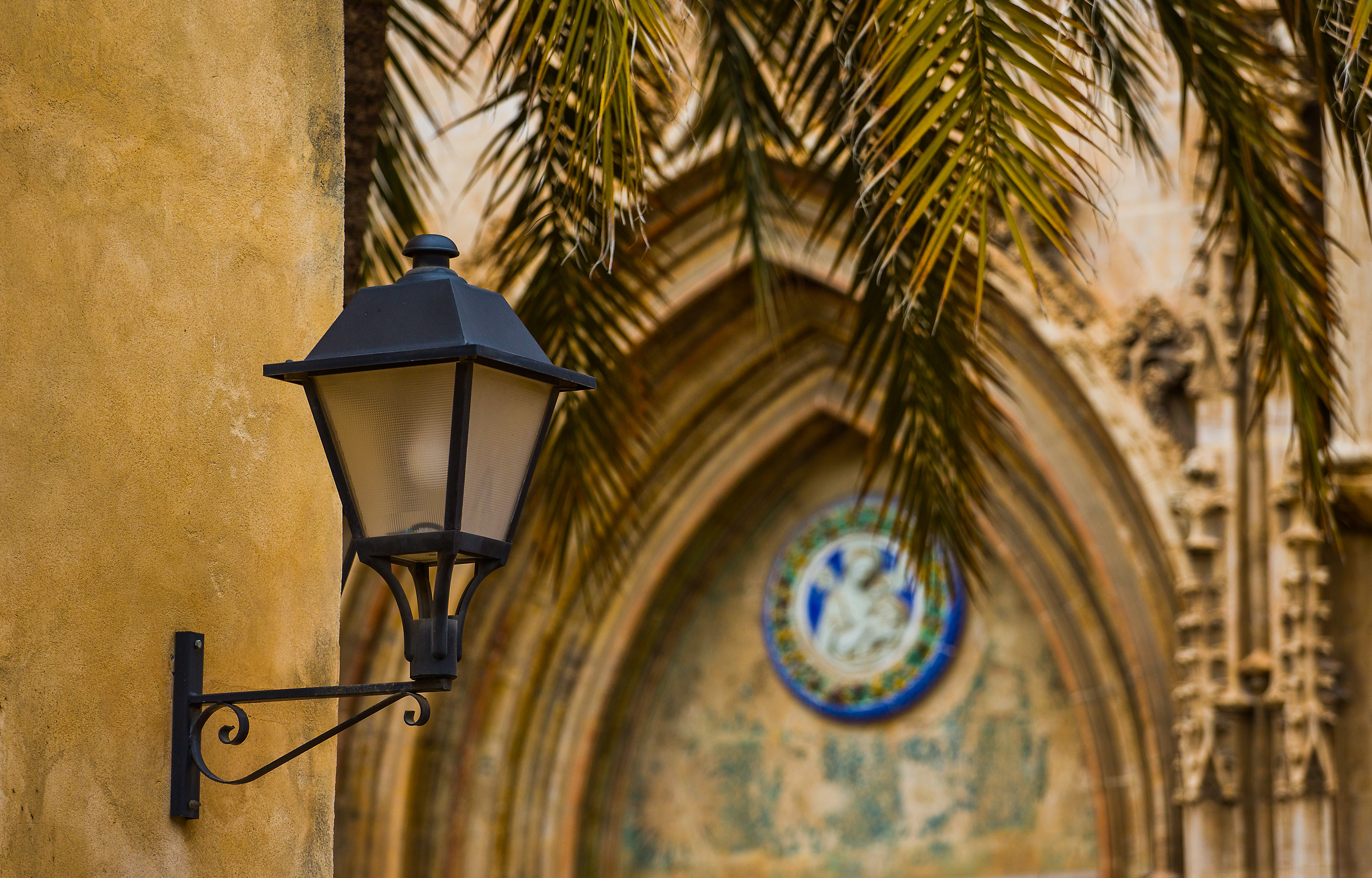 Antik lampe blandt palmetræer og kirkeportal i Valencia, Spanien