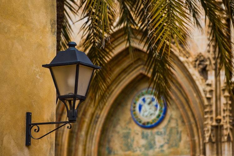 Antik lampe blandt palmetræer og kirkeportal i Valencia, Spanien