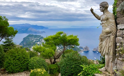 Antik romersk statue med betagende udsigt over Capri-øen og det azurblå Middelhav, omgivet af frodig grøn vegetation