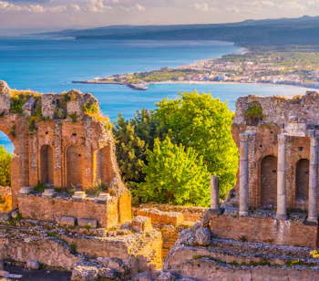 Historisk græsk teater i Taormina på Sicilien med dramatisk solnedgang over Middelhavet og Etna-vulkanen i baggrunden
