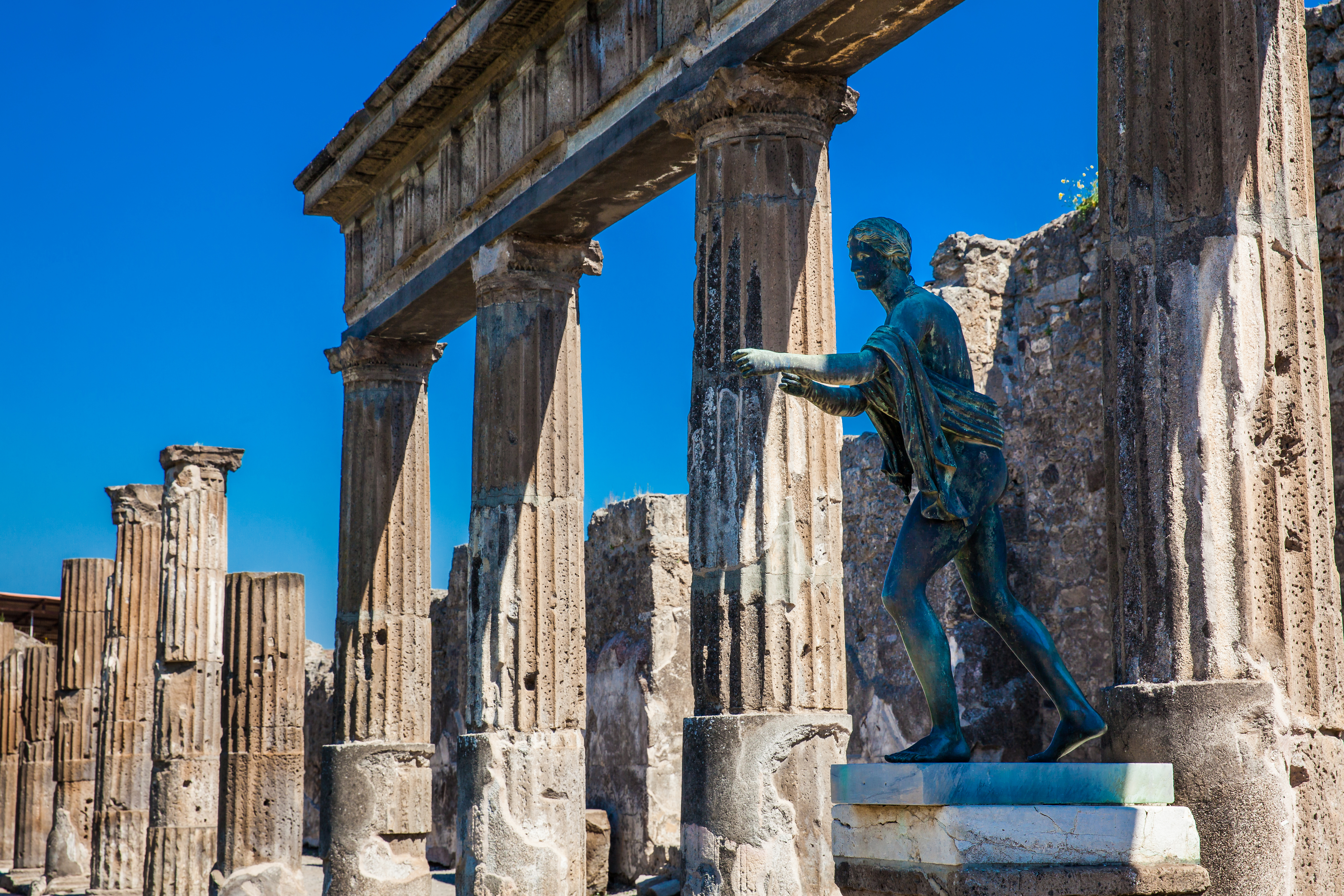 Historiske ruiner af Apollotemplet med bronzestatue i Pompeji, Italien, med Vesuv i baggrunden under blå himmel