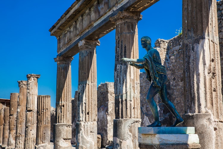 Historiske ruiner af Apollotemplet med bronzestatue i Pompeji, Italien, med Vesuv i baggrunden under blå himmel