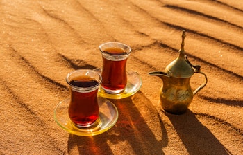 Traditionel arabisk te-ceremoni med kande og glas på gyldne sandklitter i Dubai-ørkenen ved solnedgang