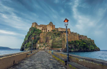Det historiske Aragonese slot på klippeø ved Ischia i Italien i aftenlys med stenbro i forgrunden