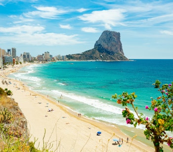 Idyllisk udsigt over Arenal-Bol stranden i Calpe med det majestætiske Ifac-klippe, azurblåt Middelhav og indbydende strandparasoller