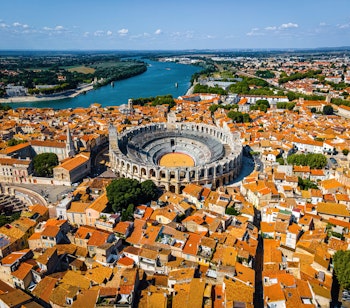 Luftfoto af Arles med det antikke romerske amfiteater omgivet af terrakottafarvede tage og Rhône-floden i Provence, Sydfrankrig
