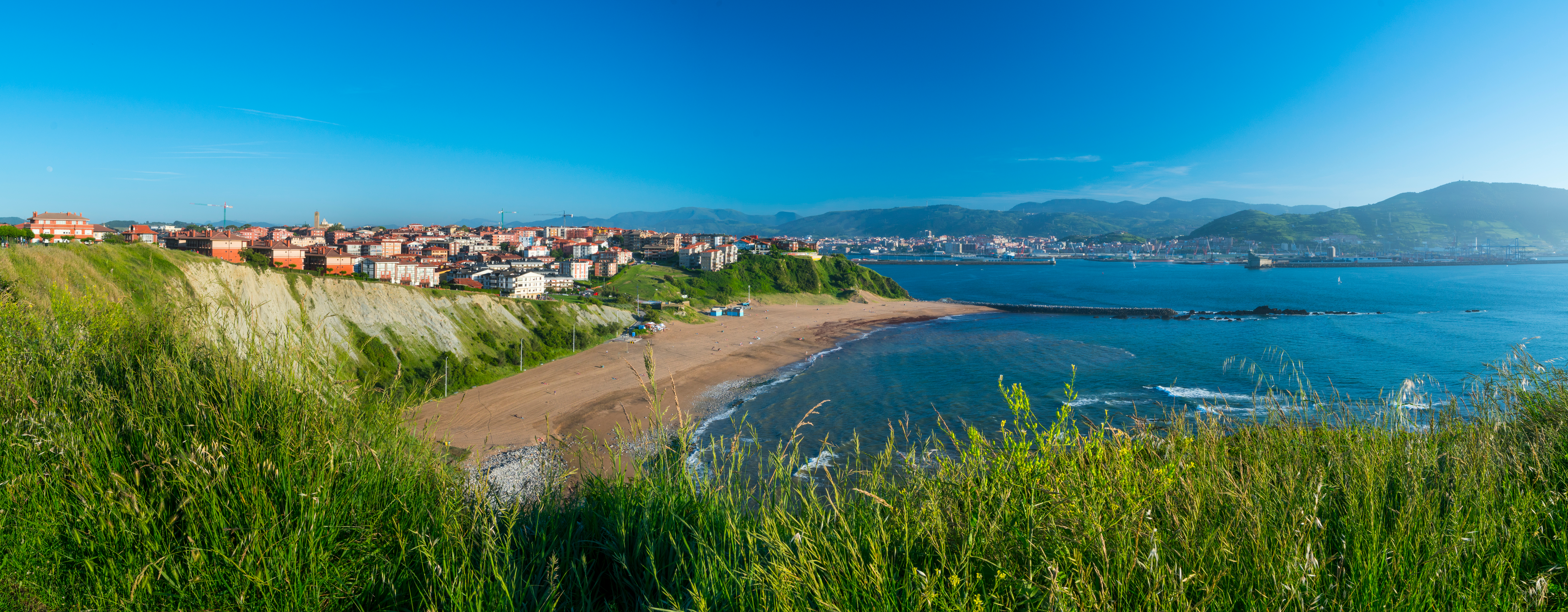Panoramaudsigt over Arrigunaga Strand i Getxo, Baskerlandet, Spanien, med turkisblåt hav, sandstrand og farverige kystbyhuse under en klar blå himmel