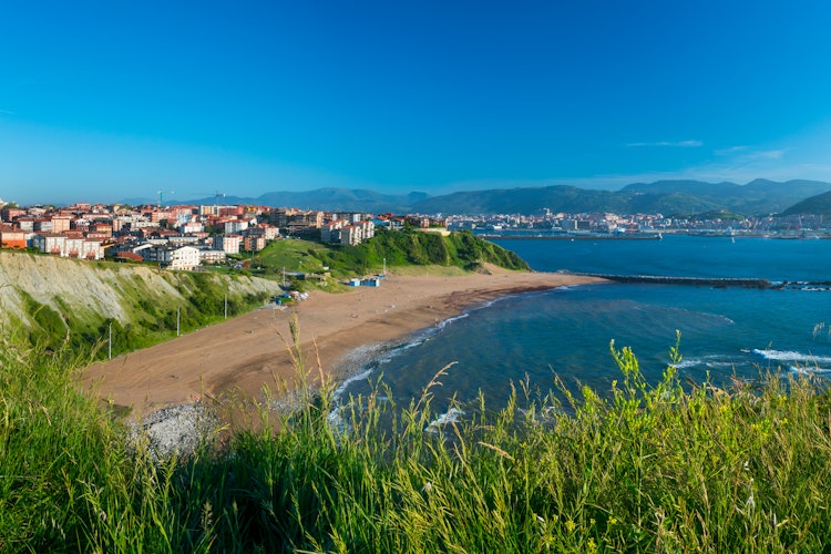 Panoramaudsigt over Arrigunaga Strand i Getxo, Baskerlandet, Spanien, med turkisblåt hav, sandstrand og farverige kystbyhuse under en klar blå himmel