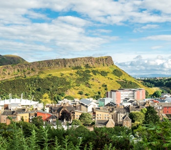Panoramaudsigt over Arthur's Seat bjerget i Edinburgh med grønne naturområder og byens skyline under blå himmel
