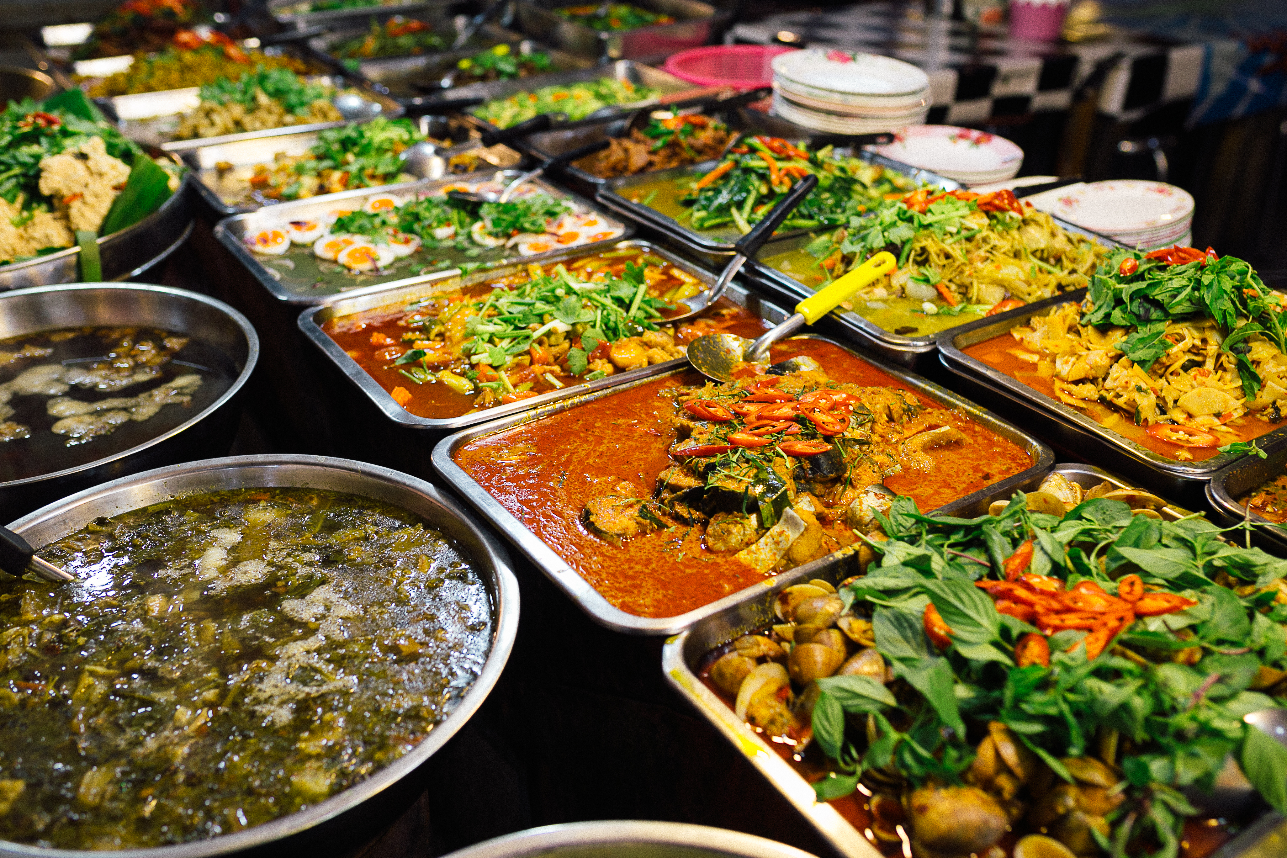 Farverige asiatiske curryretter og traditionel gadekøkkenmad serveret i metalfade på lokalt marked